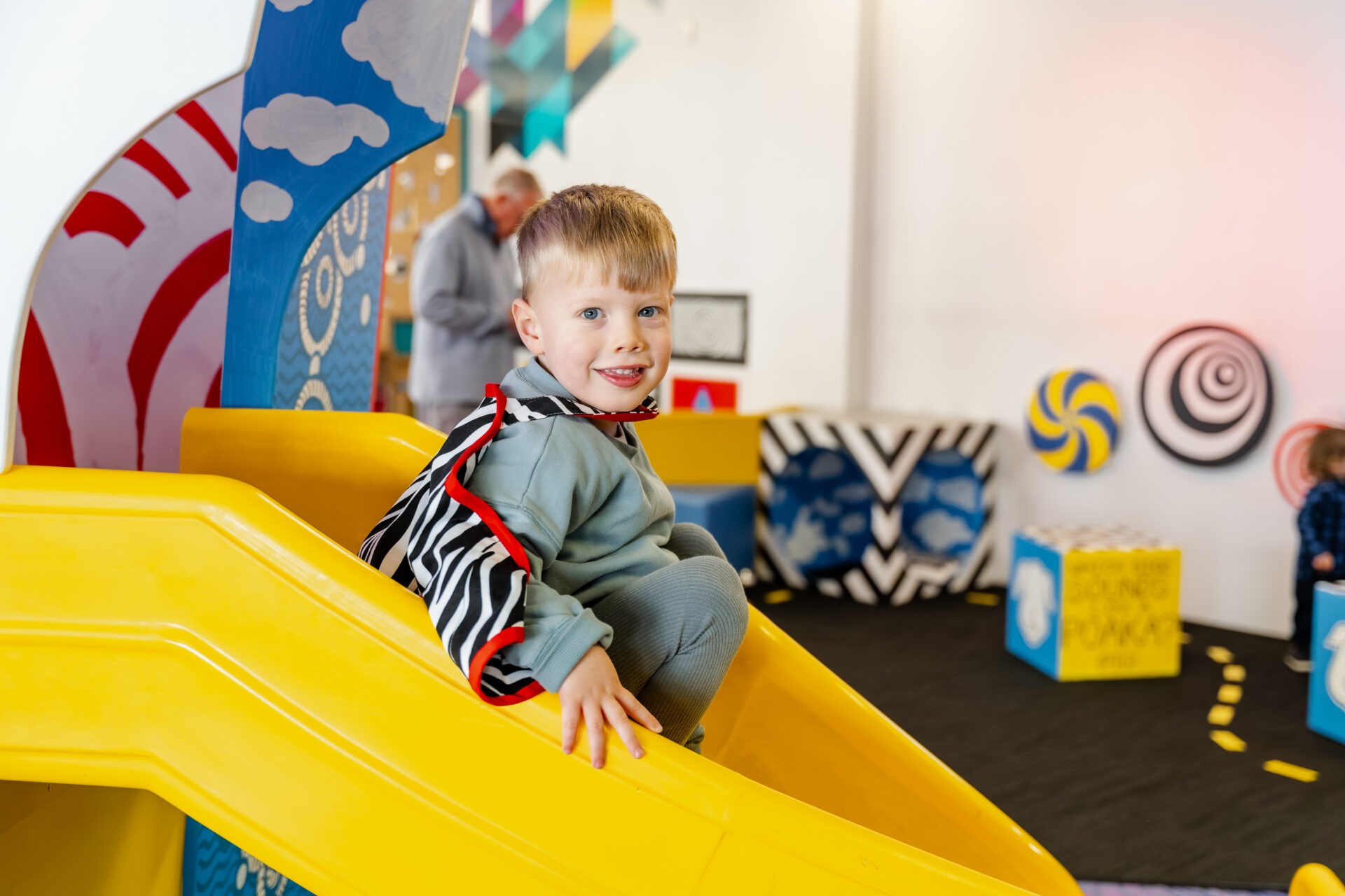 A boy sitting on the slide in PlayHQ, wearing a costume.