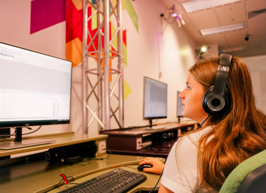 A girl wearing headphones, using a computer to make digital music