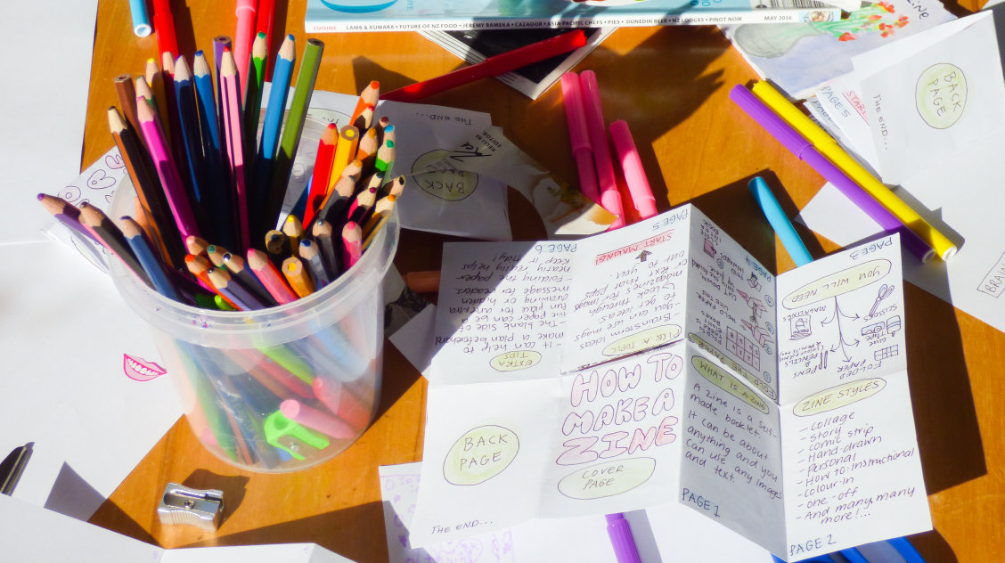 A craft table with zines and colouring pencils on it